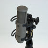 This is a photo of the Sanken CU-55 microphone. It is shown in a grey colour. It is held in place by a piece of black equipment at an angled front view.
